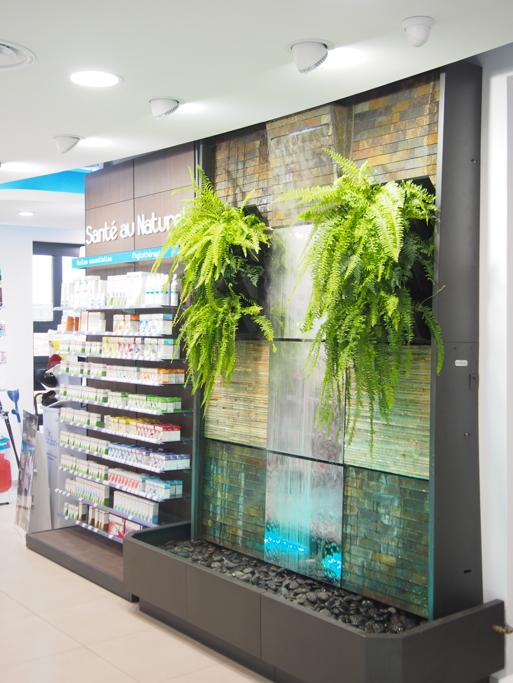 Mur d’eau et comptoirs en verre – design naturel et chaleureux de la pharmacie Mathieu