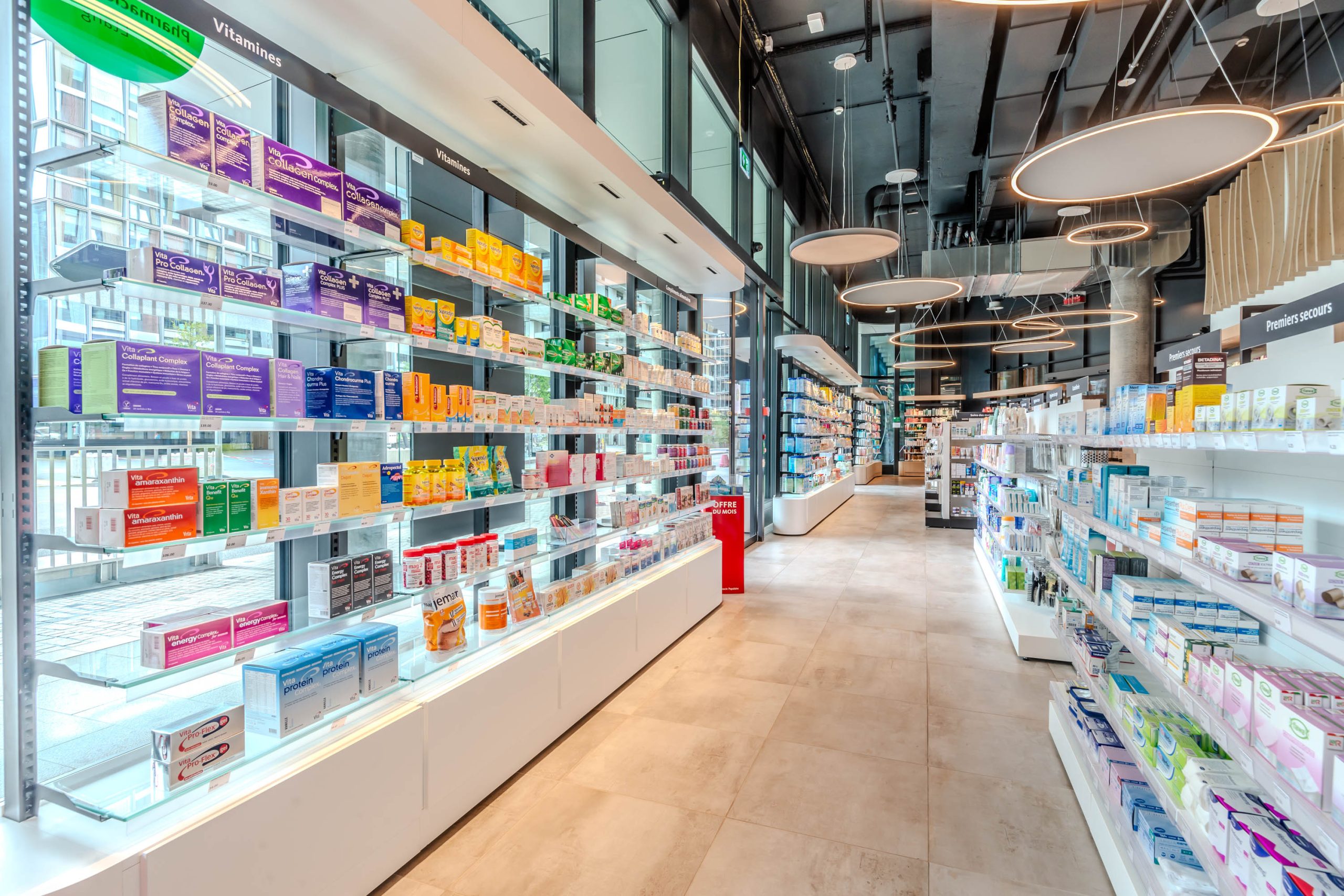 Linéaires et gondoles. Pharmacie Populaire Etang. Plafond technique noir. Luminaires majestueux