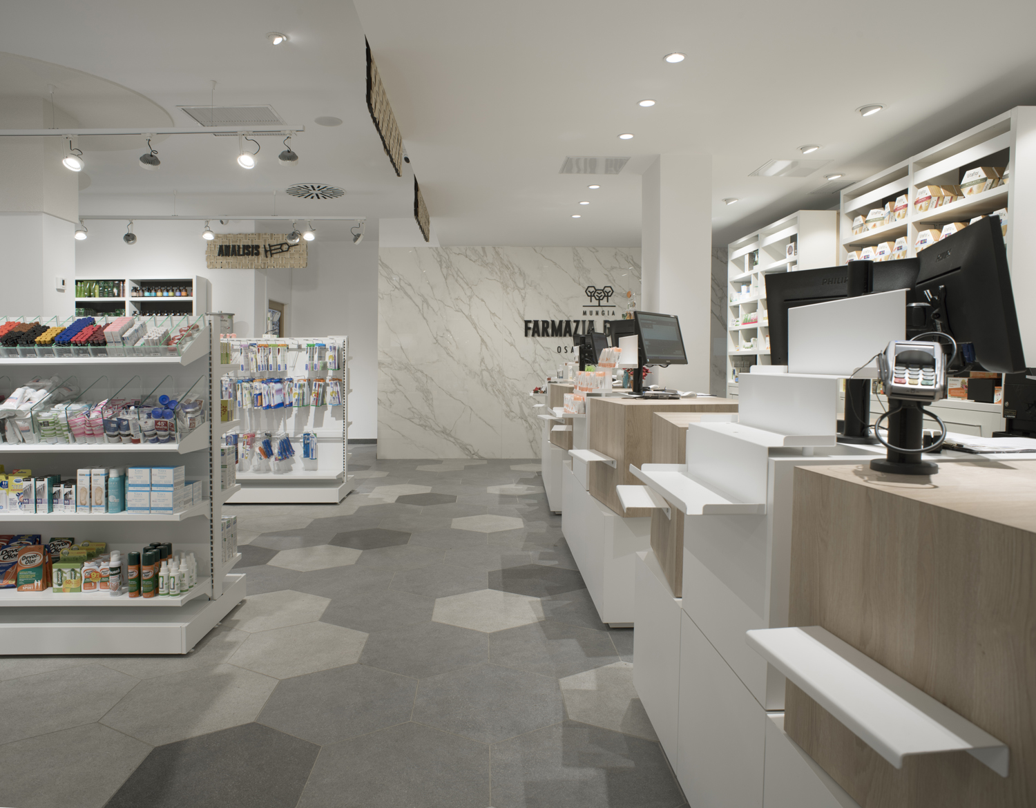 Mostradores blancos y madera, pared de mármol y suelo hexagonal en la Farmacia Golzarri, Mungia.