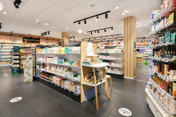 Vue d’ensemble de l’espace de vente réagencé de la Pharmacie du Collège, mêlant bois naturel, éclairage doux et parcours client fluide.