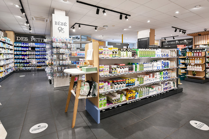 Vue d’ensemble de l’espace de vente réagencé de la Pharmacie du Collège, mêlant bois naturel, éclairage doux et parcours client fluide.