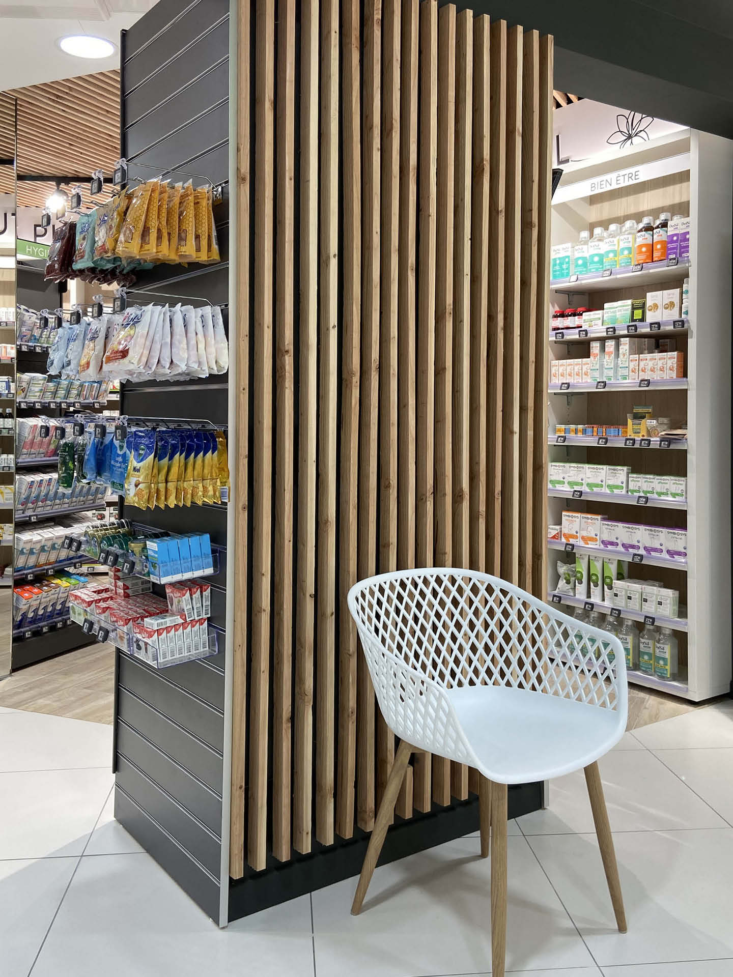 Chaise devant un mur en tasseaux de bois dans la Pharmacie Escarra à Cabestany, créant un espace d’attente chaleureux et naturel, reflet du nouvel aménagement de l’officine.