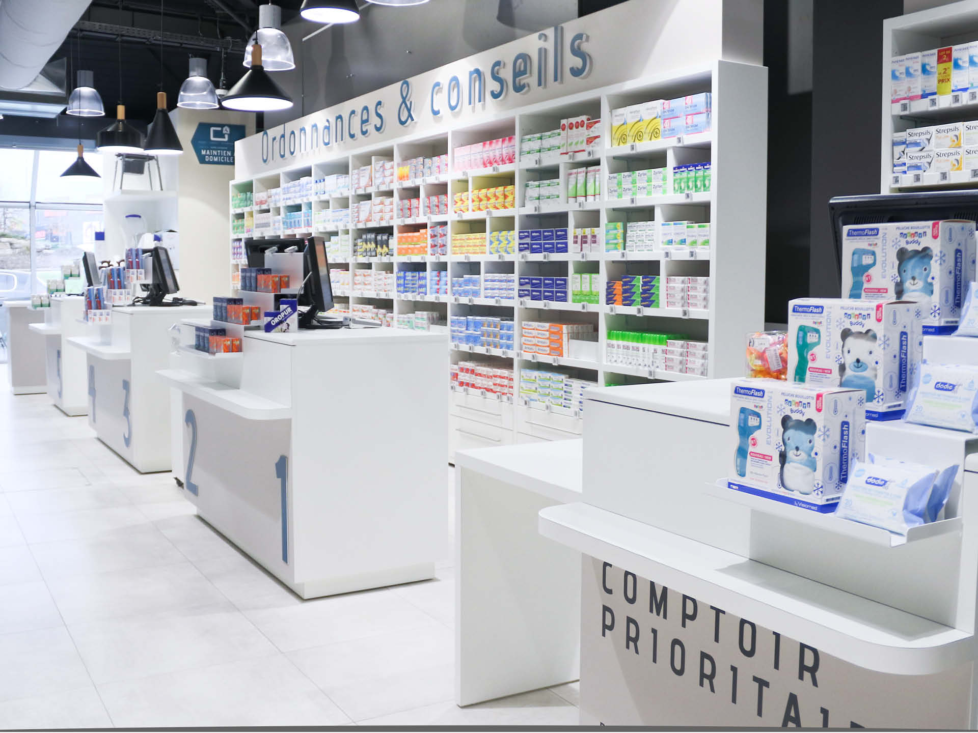 Comptoirs blancs sur-mesure, accompagnés d’un plafond graphique noir et d’un jeu de lumières.