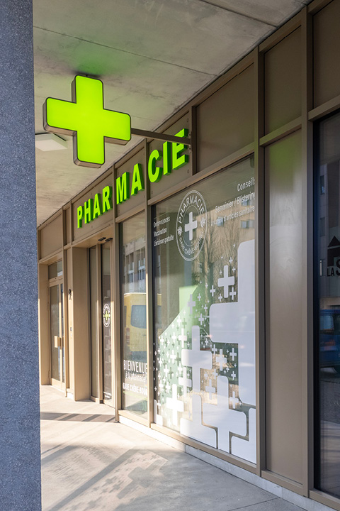 Façade moderne de la Pharmacie Gare Chêne-Bourg à Genève, située face à la gare, avec signalétique claire et vitrophanie illustrant un train.
