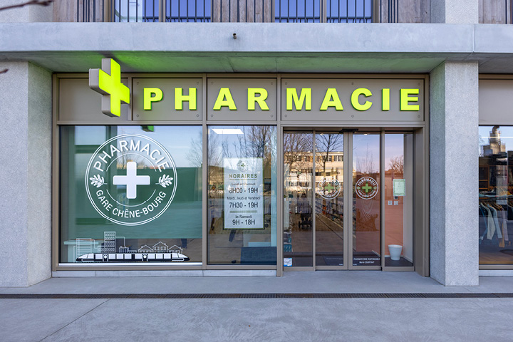Façade moderne de la Pharmacie Gare Chêne-Bourg à Genève, située face à la gare, avec signalétique claire et vitrophanie illustrant un train.