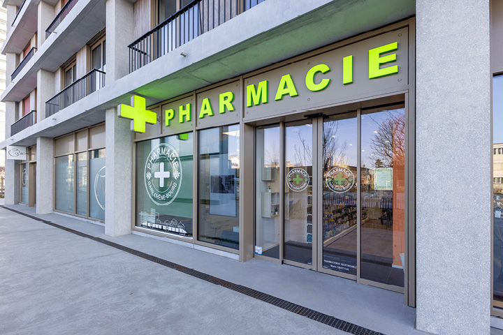Façade moderne de la Pharmacie Gare Chêne-Bourg à Genève, située face à la gare, avec signalétique claire et vitrophanie illustrant un train.