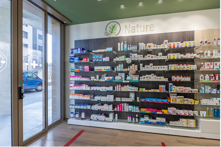 Vue d’ensemble de l’espace de vente de la Pharmacie Gare Chêne-Bourg, agencé en longueur avec des tons bois, vert et orange pour une ambiance chaleureuse.
