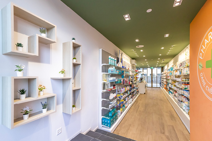 Vue d’ensemble de l’espace de vente de la Pharmacie Gare Chêne-Bourg, agencé en longueur avec des tons bois, vert et orange pour une ambiance chaleureuse.