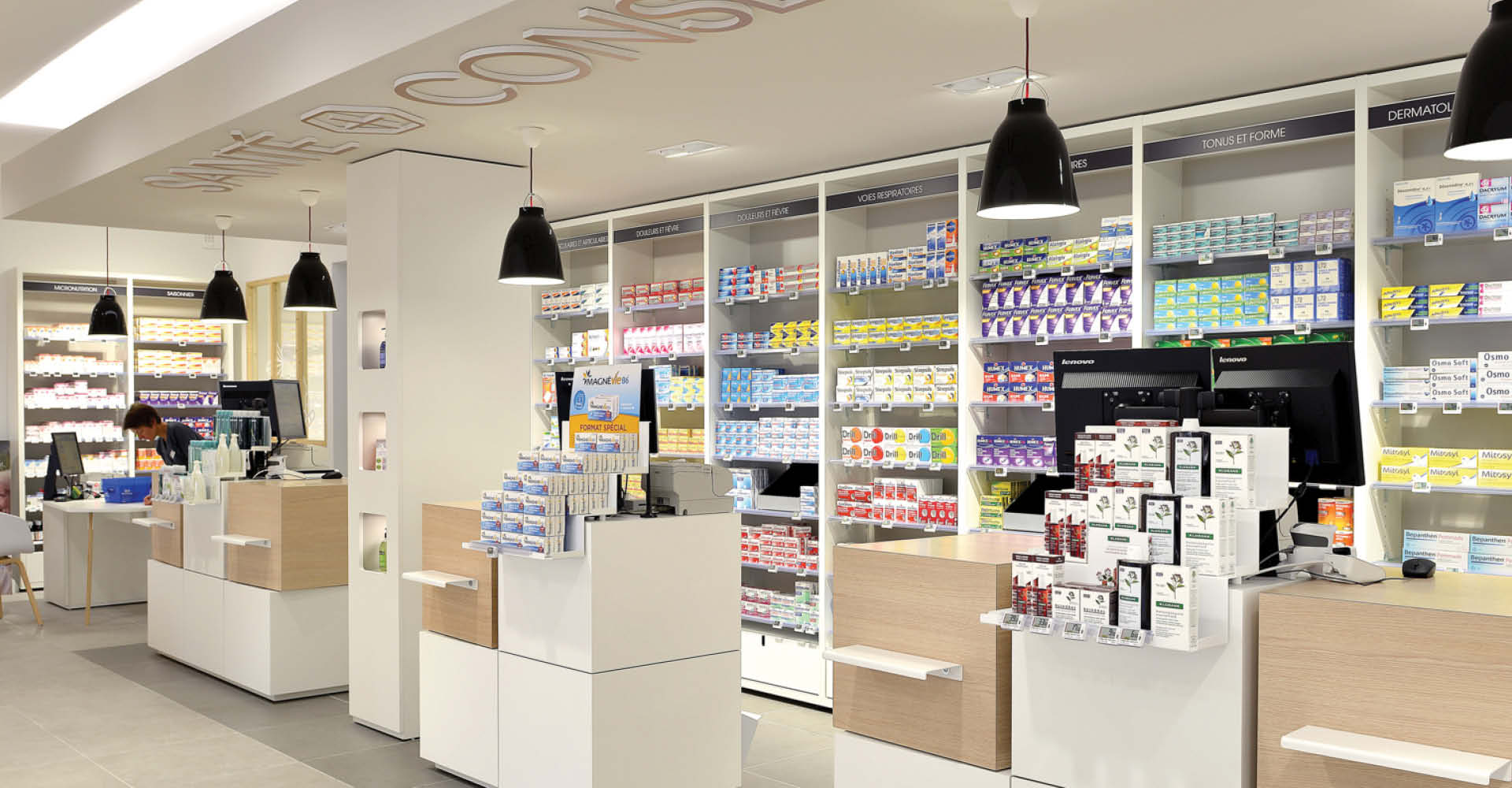 Zone comptoirs avec aménagement intérieur de la pharmacie du Pays de Retz, design épuré en bois clair et blanc, espace lumineux et naturel favorisant le bien-être des patients.