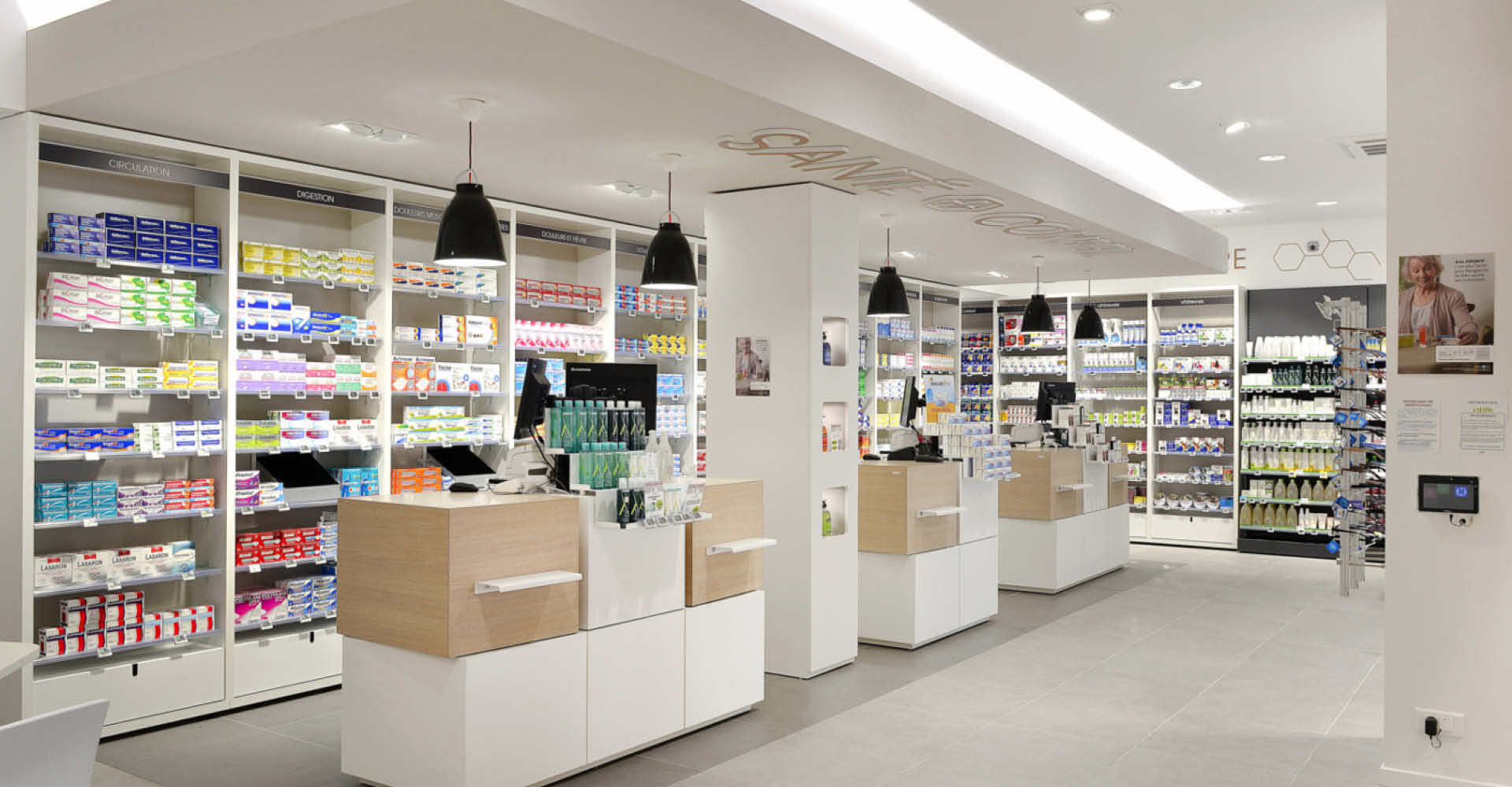Zone comptoirs avec aménagement intérieur de la pharmacie du Pays de Retz, design épuré en bois clair et blanc, espace lumineux et naturel favorisant le bien-être des patients.