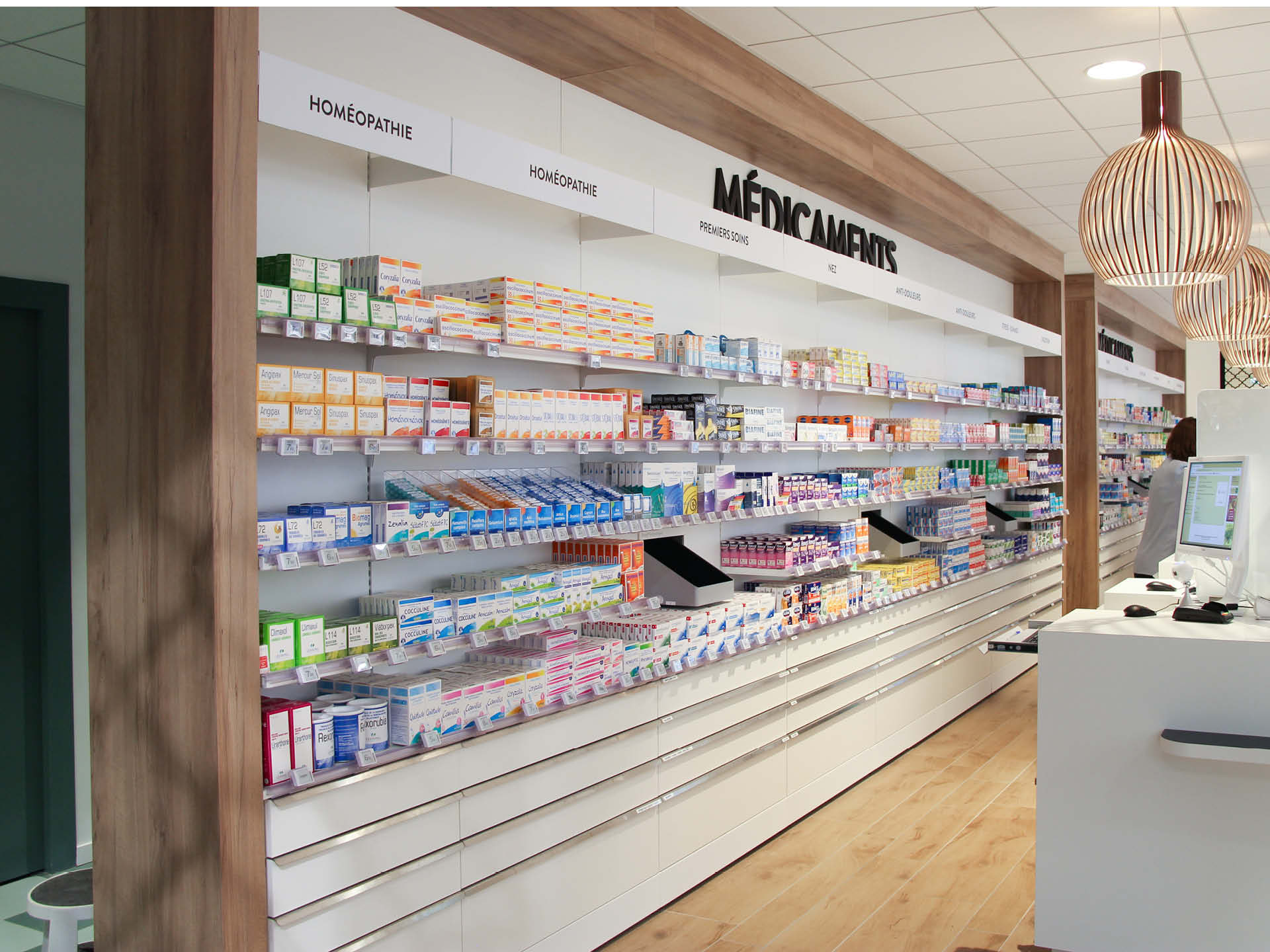 Espace comptoir mis en avant via de la signalétique et des luminaires en bois pour apporter de la chaleur dans la pharmacie.
