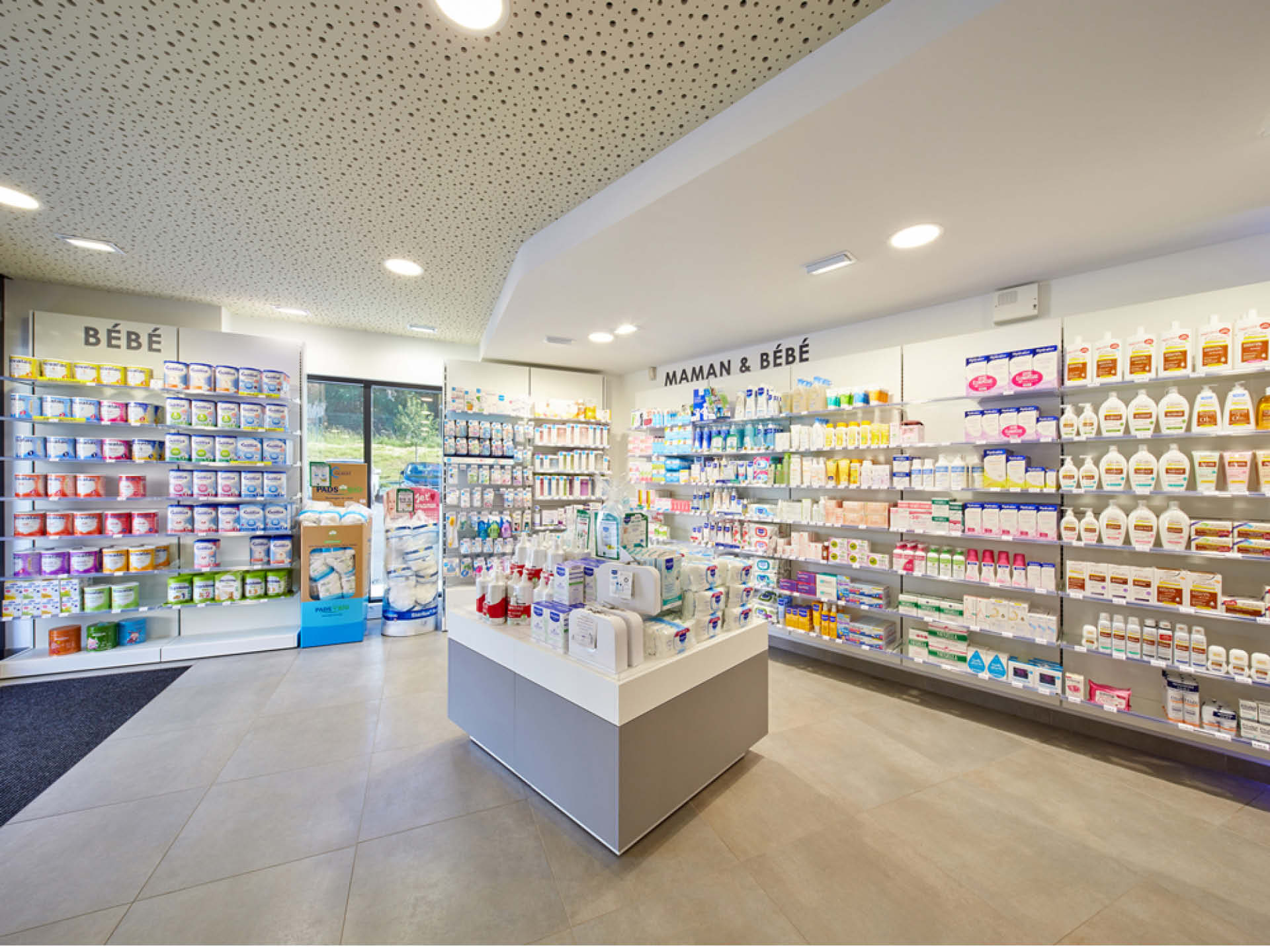 Espace bébé et maman mis en valeur par un plafond en blanc avec une mise en scène dasn l'agencement d ela pharmacie via un mobilir su-mesure.