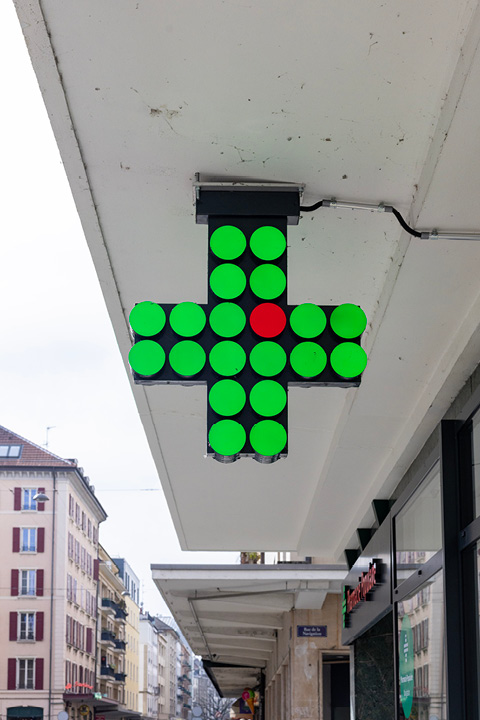 Croix verte lumineuse emblématique de la Pharmacie Populaire sur la façade, symbole de l’officine.