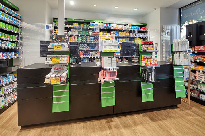 Comptoirs noirs et verre élégants de la Pharmacie du 20ᵉ à Paris, combinant modernité et transparence pour valoriser la zone de délivrance et renforcer l’image haut de gamme de l’officine.
