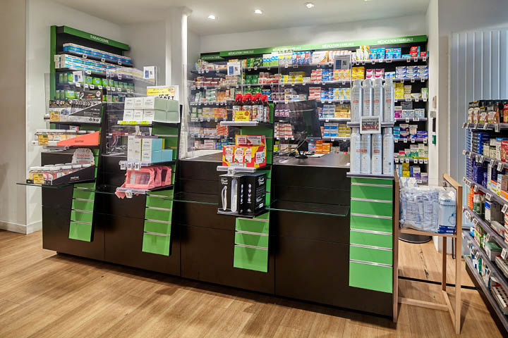 Comptoirs noirs et verre élégants de la Pharmacie du 20ᵉ à Paris, combinant modernité et transparence pour valoriser la zone de délivrance et renforcer l’image haut de gamme de l’officine.