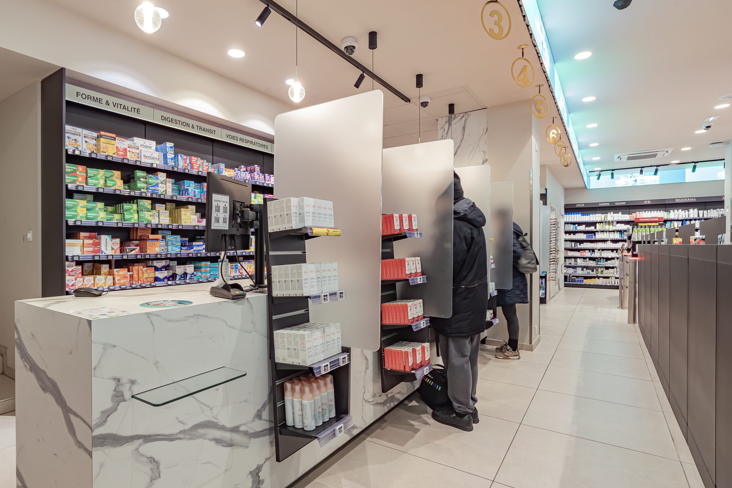 Intérieur moderne de la pharmacie du Dôme avec comptoir en marbre et rayons de médicaments ORL, ophtalmologie et circulation.