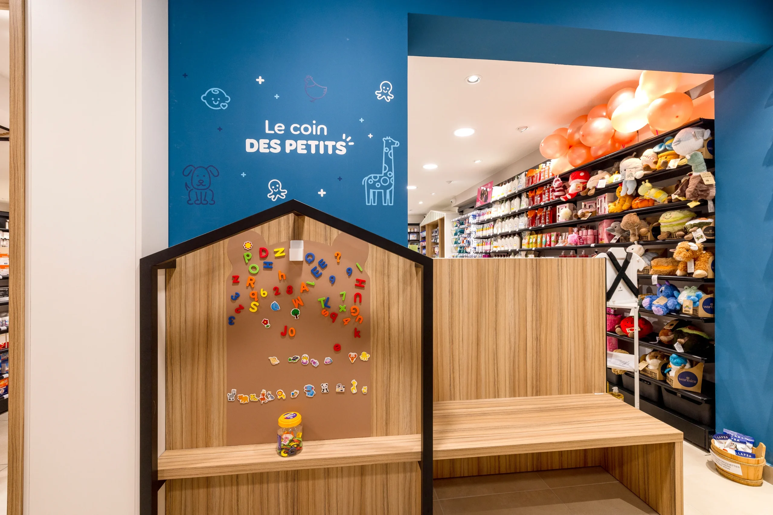 Coin des petits de la Pharmacie du Golfe avec cabane en bois, jeu mural et banc pour les enfants.