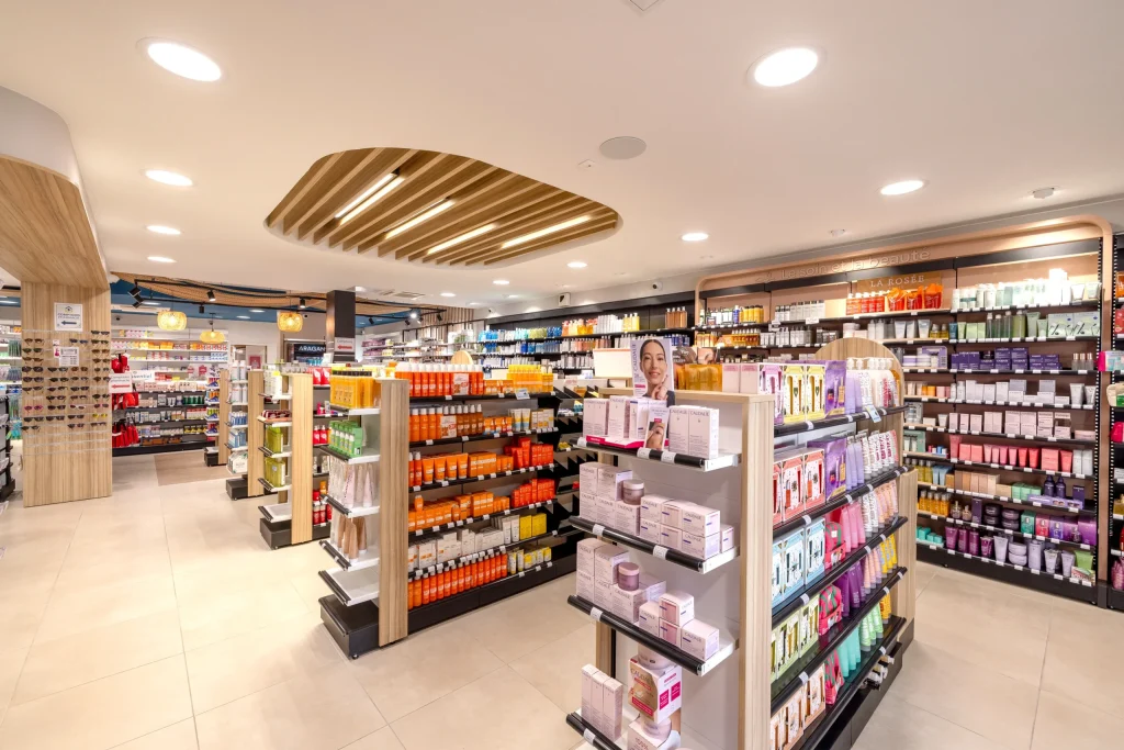 Vue générale de l’espace de vente de la Pharmacie du Golfe avec plafond bois suspendu et gondoles sur-mesure.
