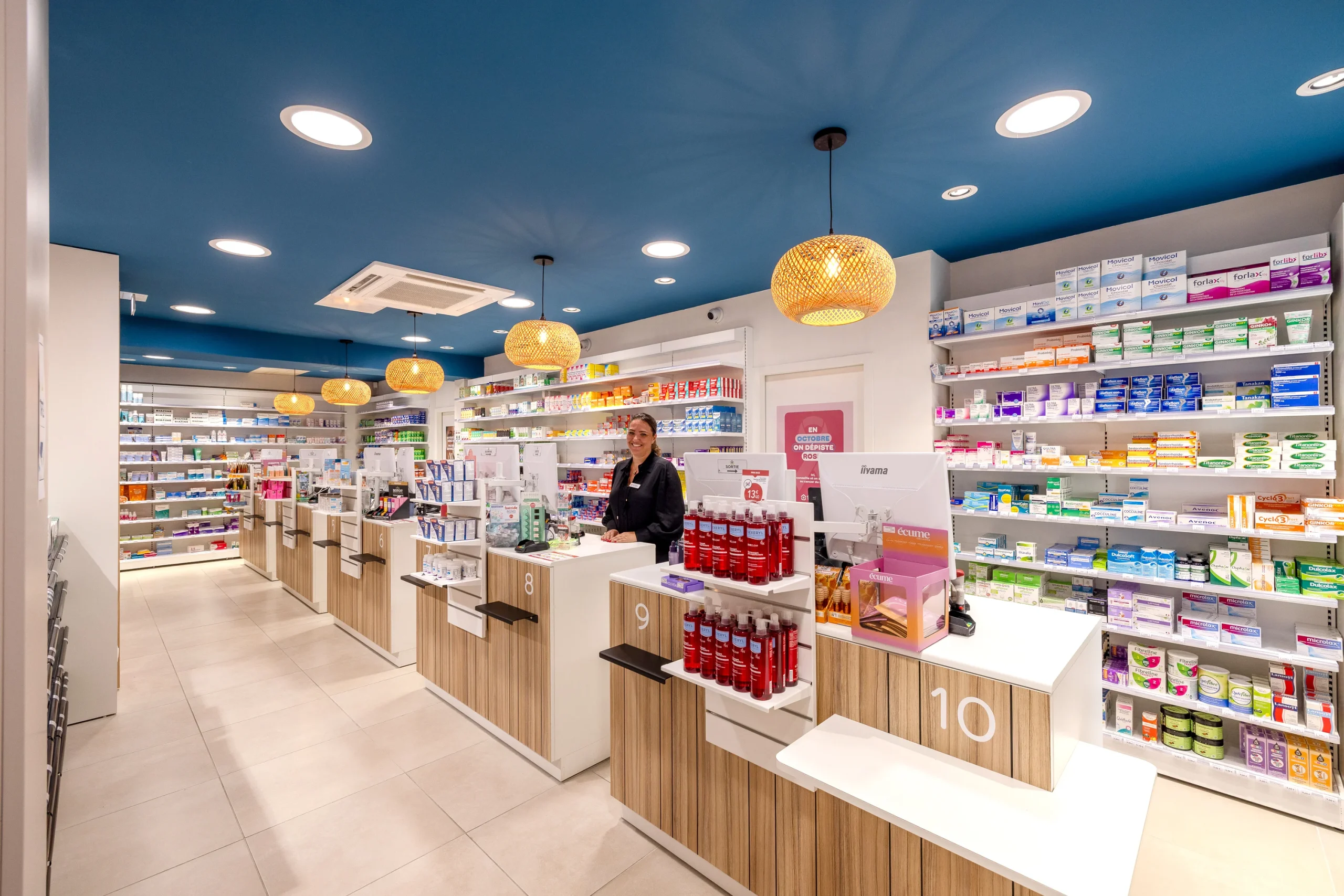 Vue en enfilade des comptoirs de la Pharmacie du Golfe avec une pharmacienne au conseil.