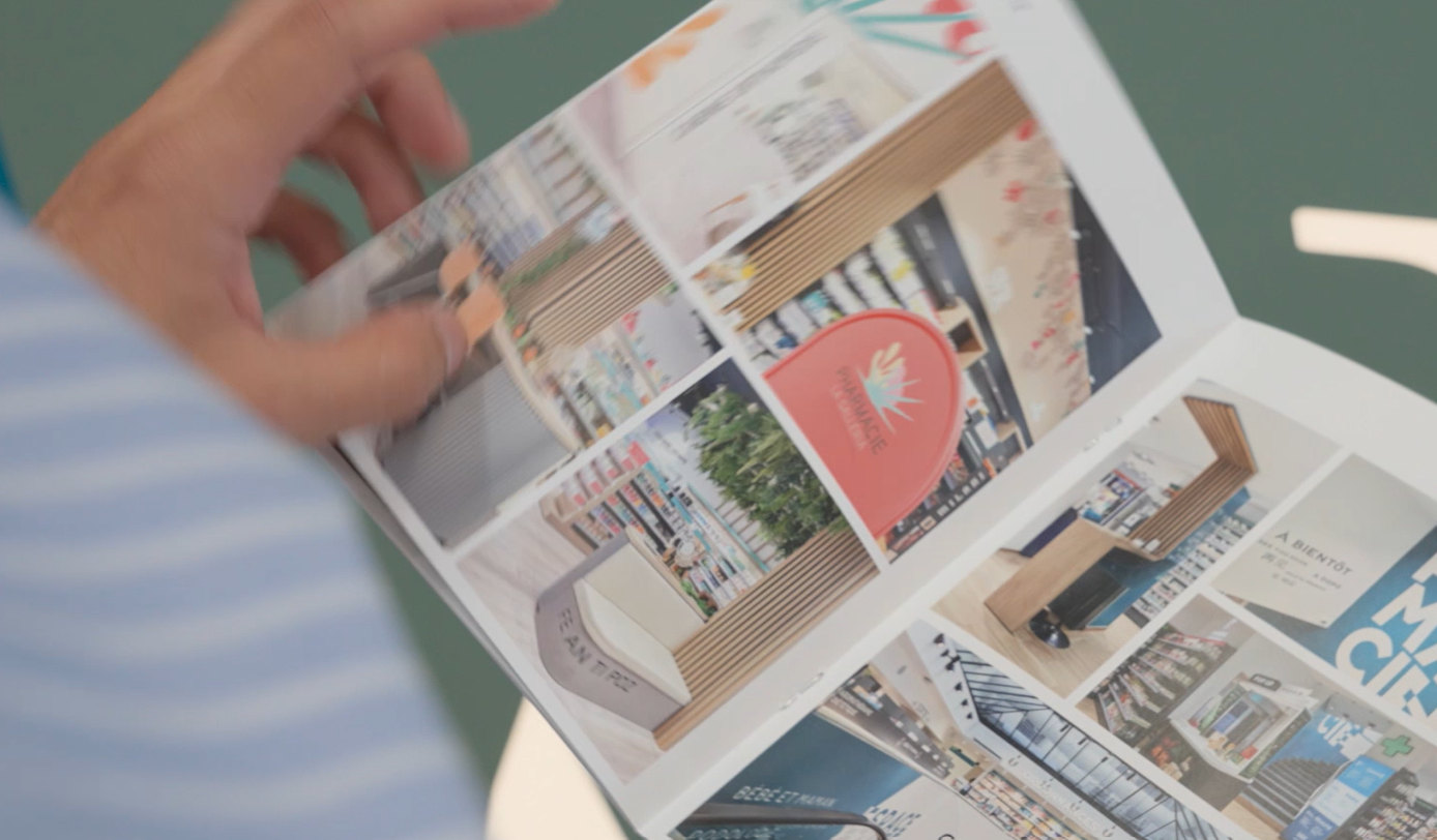 Personne feuilletant une brochure Mobil M présentant différents concepts d'agencement et de design intérieur de pharmacies avec des mobiliers modernes.