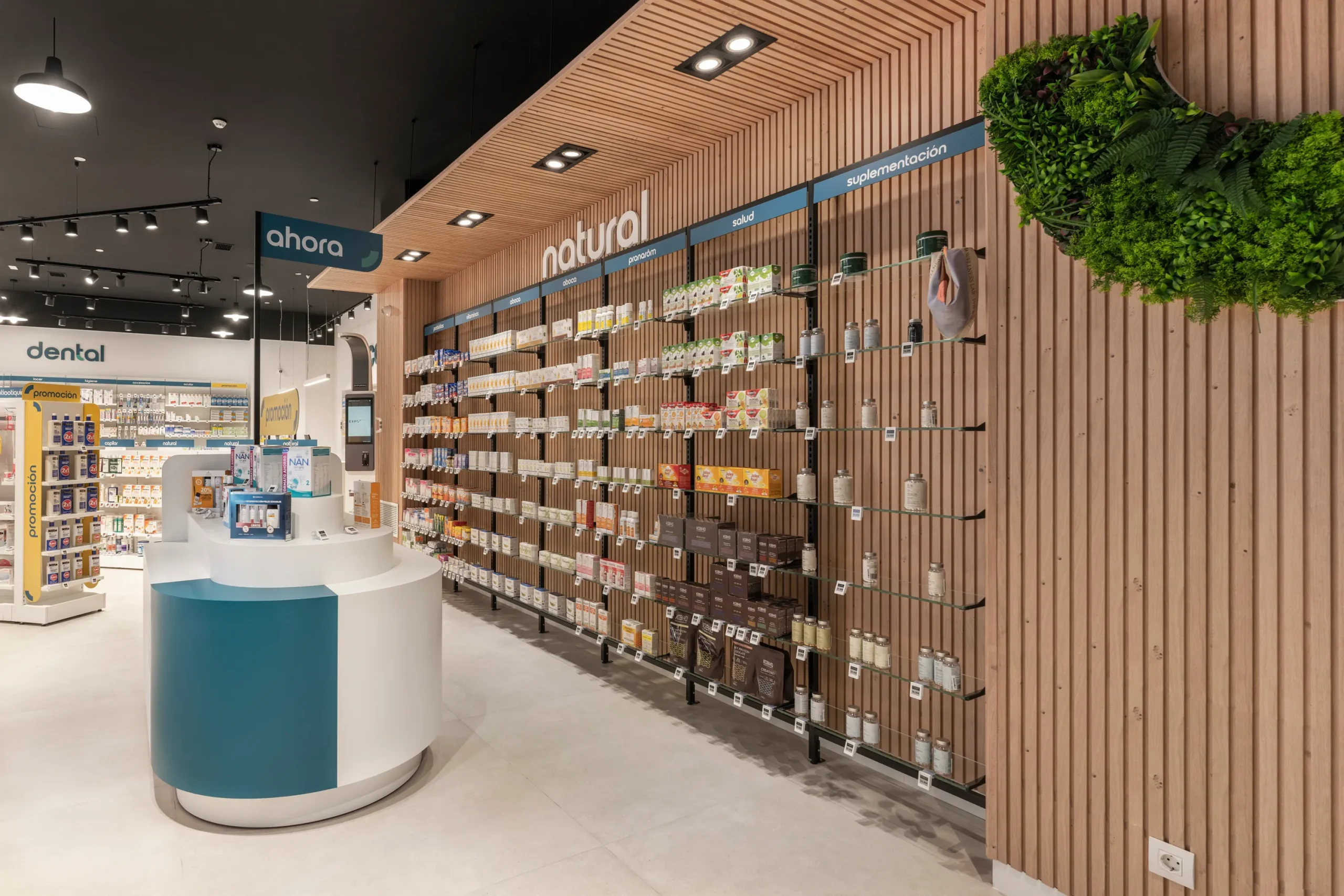 Sección natural de farmacia con panelado de madera, jardín vertical integrado y mueble isla turquesa.